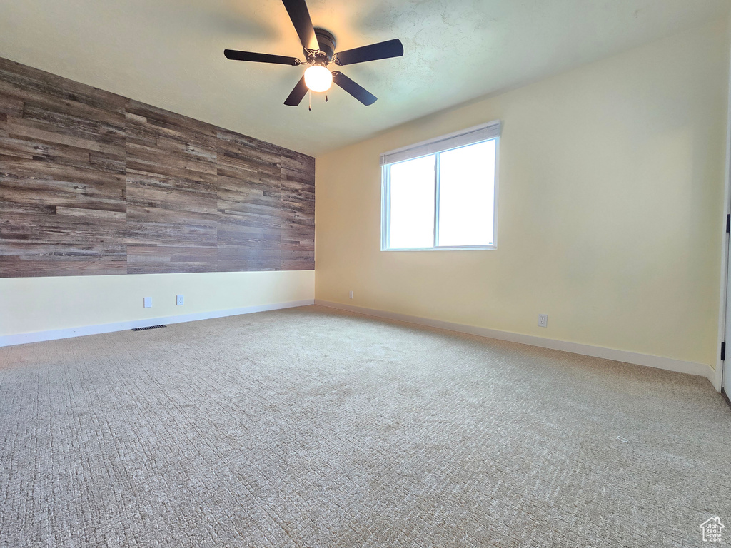Spare room featuring ceiling fan, wooden walls, and carpet floors