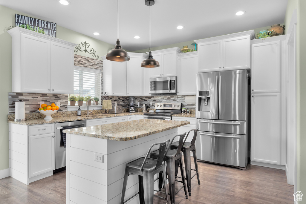 Kitchen with a kitchen island, wood-type flooring, backsplash, and stainless steel appliances