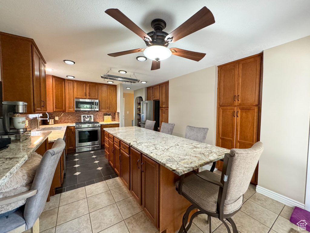 Kitchen with appliances with stainless steel finishes, backsplash, ceiling fan, and light tile floors