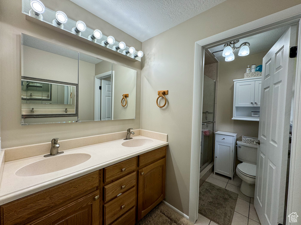 Bathroom with oversized vanity, toilet, tile flooring, a textured ceiling, and double sink