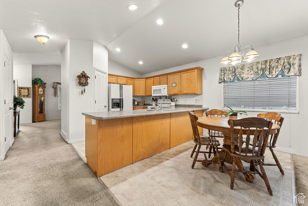 Kitchen with light tile floors, white appliances, decorative light fixtures, vaulted ceiling, and kitchen peninsula