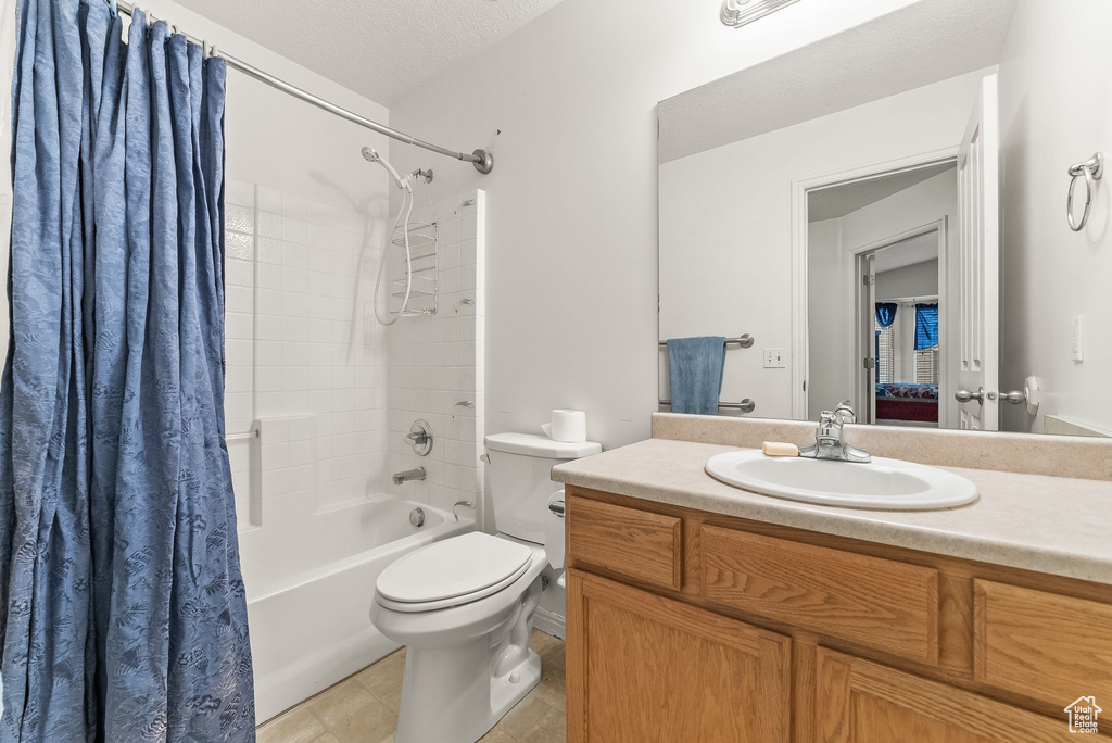 Full bathroom featuring shower / tub combo, vanity with extensive cabinet space, toilet, tile flooring, and a textured ceiling