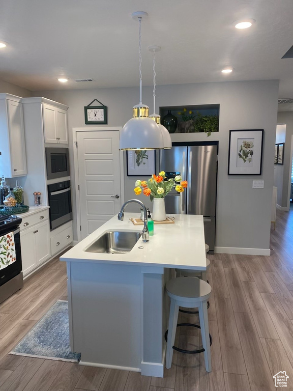 Kitchen featuring white cabinets, light hardwood / wood-style floors, a kitchen island with sink, and appliances with stainless steel finishes