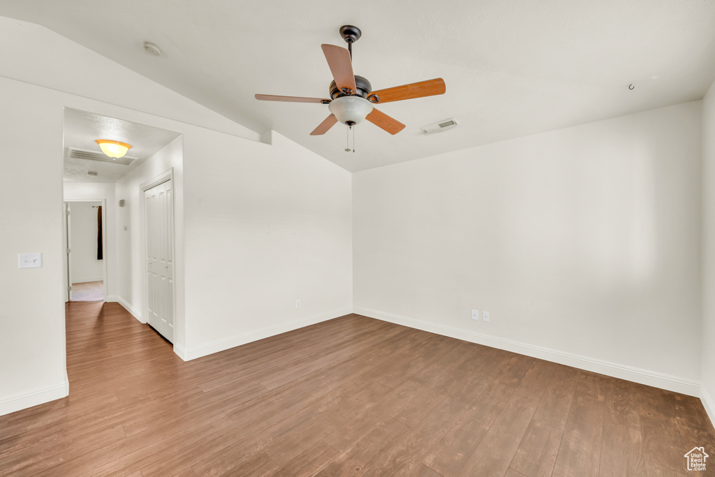 Spare room featuring wood-type flooring, ceiling fan, and vaulted ceiling