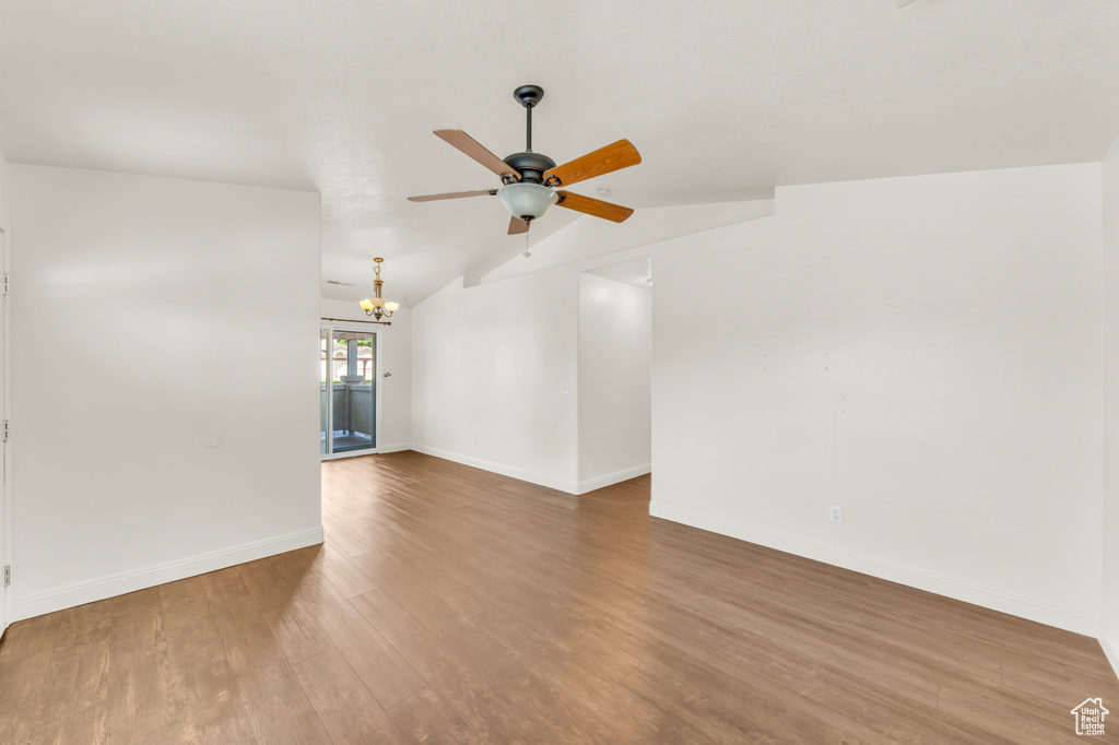 Empty room featuring lofted ceiling, wood-type flooring, and ceiling fan with notable chandelier