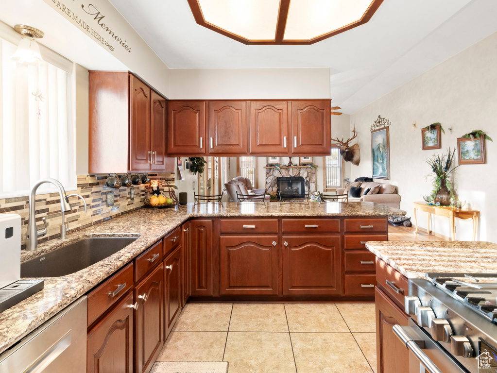 Kitchen featuring sink, light tile flooring, backsplash, stainless steel dishwasher, and light stone countertops