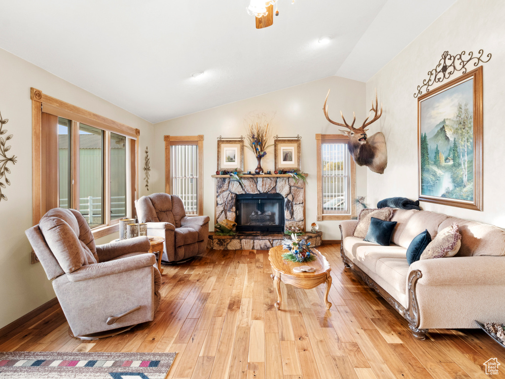 Living room featuring vaulted ceiling, hardwood / wood-style flooring, and a stone fireplace