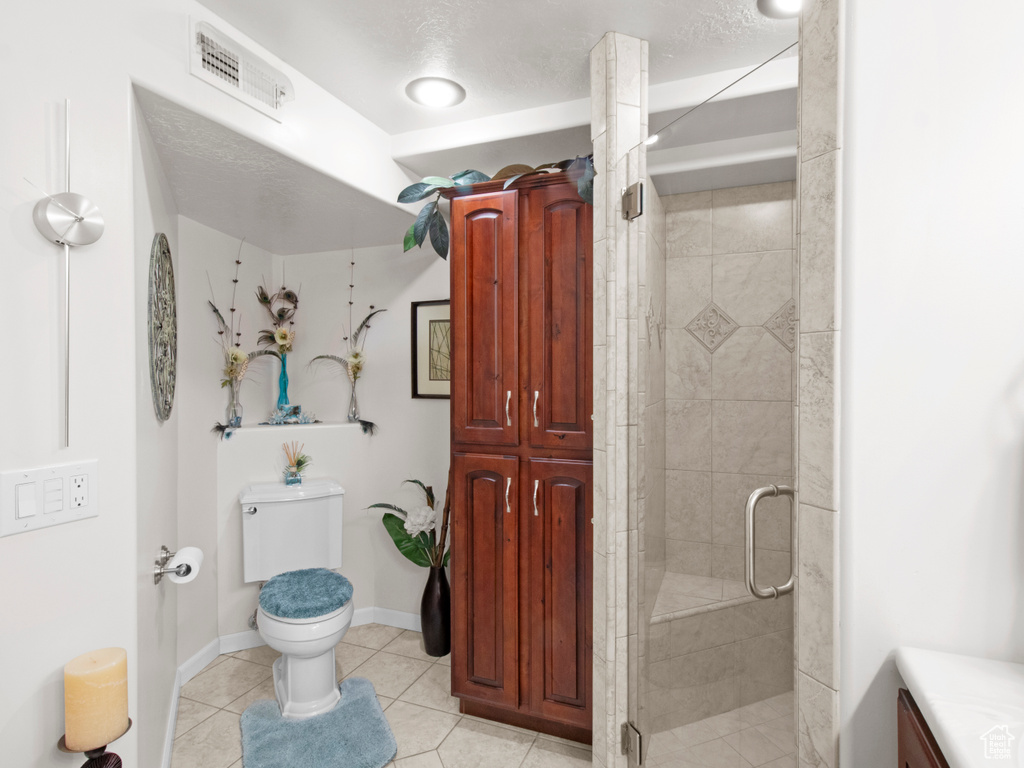 Bathroom with an enclosed shower, toilet, tile flooring, and vanity