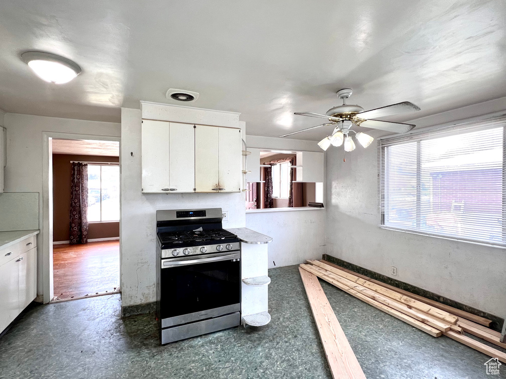 Kitchen with white cabinets, stainless steel gas stove, ceiling fan, and dark wood-type flooring