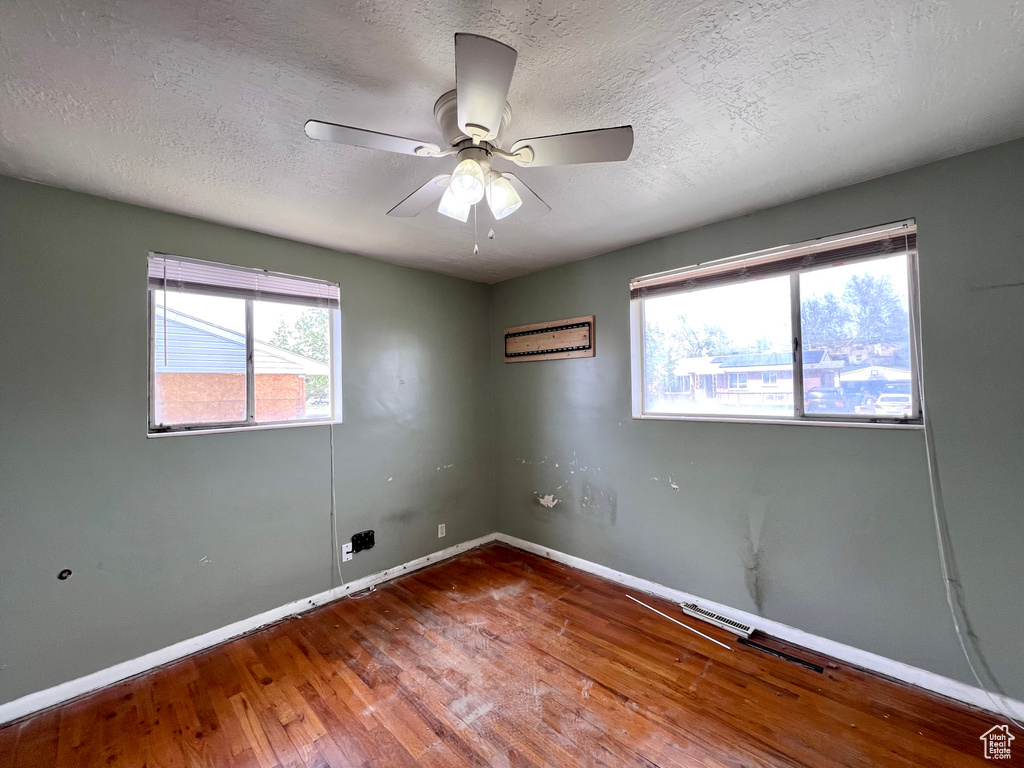 Empty room featuring plenty of natural light, dark hardwood / wood-style flooring, ceiling fan, and a textured ceiling
