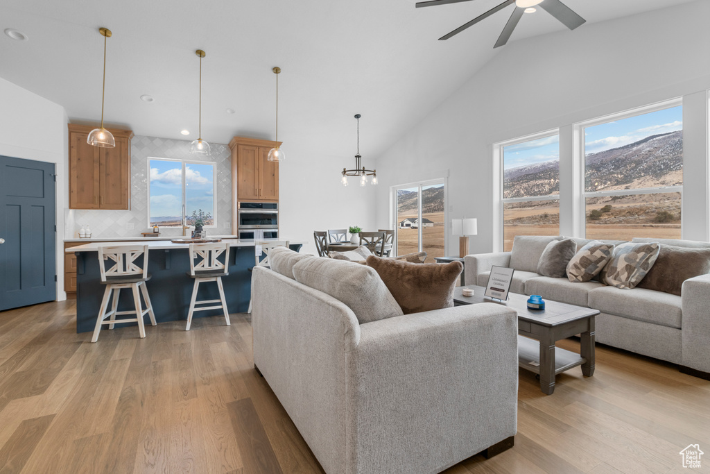 Living area featuring ceiling fan with notable chandelier, high vaulted ceiling, light wood-type flooring, and recessed lighting