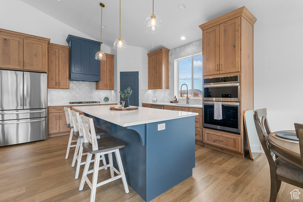 Kitchen with a sink, light wood-style floors, light countertops, appliances with stainless steel finishes, and a center island