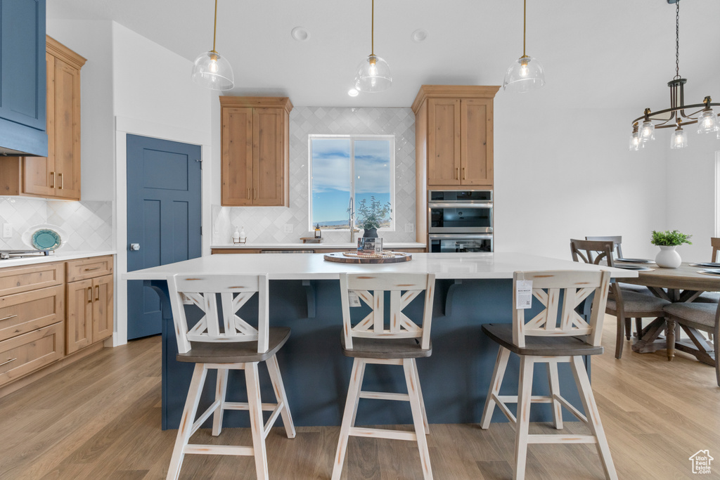 Kitchen with double oven, light wood-type flooring, light countertops, and light brown cabinetry