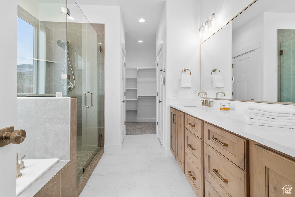 Bathroom with a relaxing tiled tub, marble finish floor, a walk in closet, vanity, and a shower stall