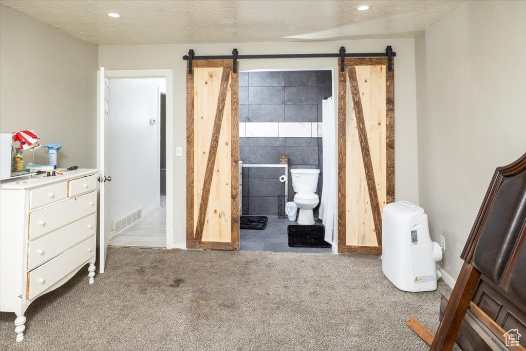 Bedroom featuring connected bathroom, tile walls, a barn door, and carpet floors