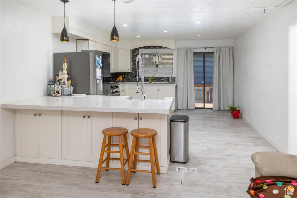 Kitchen featuring pendant lighting, light wood-type flooring, stainless steel refrigerator, kitchen peninsula, and tasteful backsplash