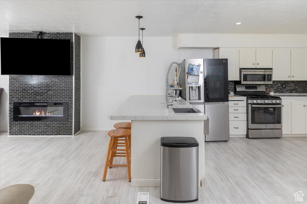 Kitchen featuring appliances with stainless steel finishes, light hardwood / wood-style floors, a large fireplace, white cabinetry, and pendant lighting