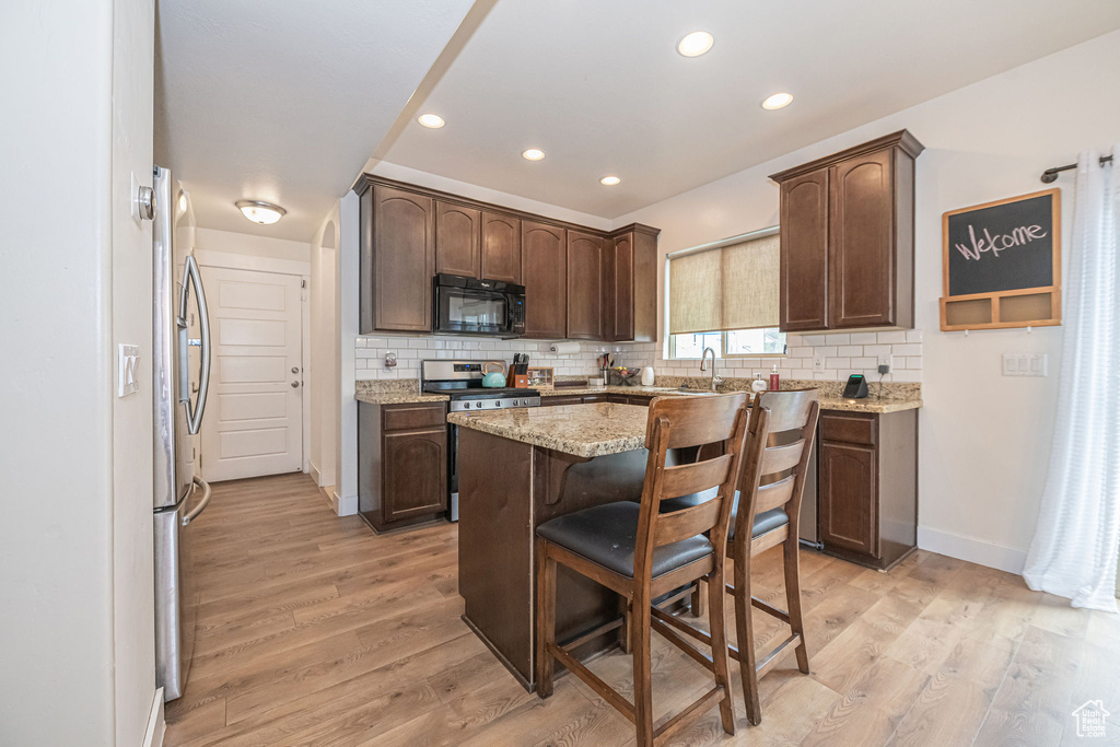 Kitchen featuring dark brown cabinets, light stone countertops, backsplash, stainless steel appliances, and light hardwood / wood-style floors