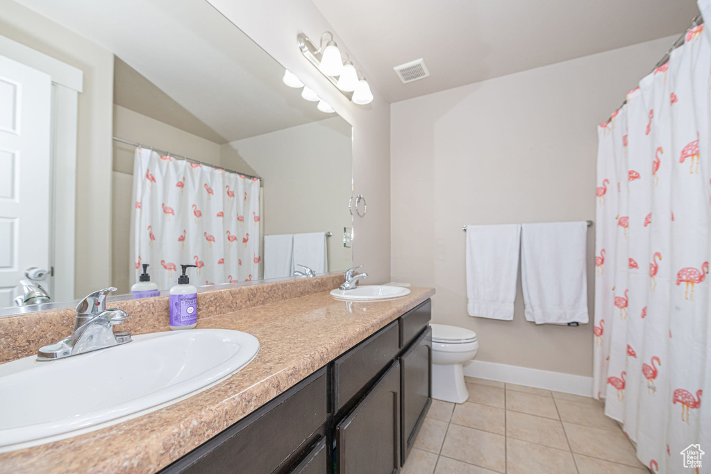 Bathroom featuring vanity with extensive cabinet space, double sink, toilet, and tile flooring