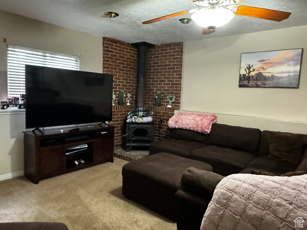 Carpeted living room with brick wall, ceiling fan, and a wood stove