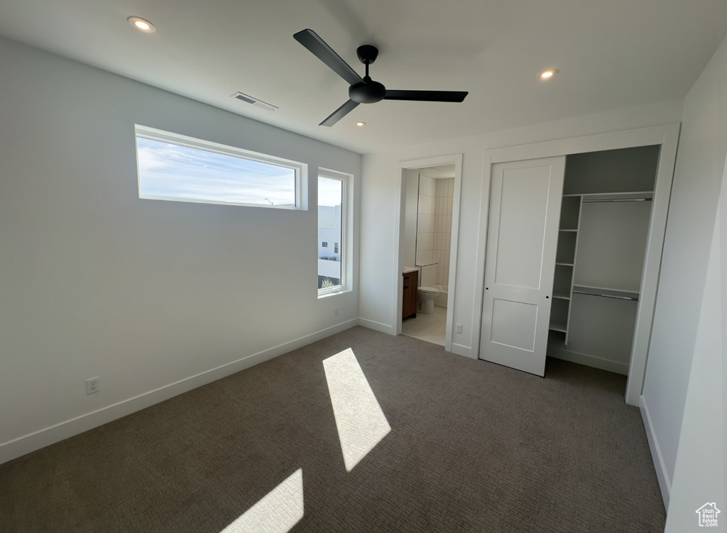 Unfurnished bedroom with a closet, connected bathroom, ceiling fan, and dark carpet