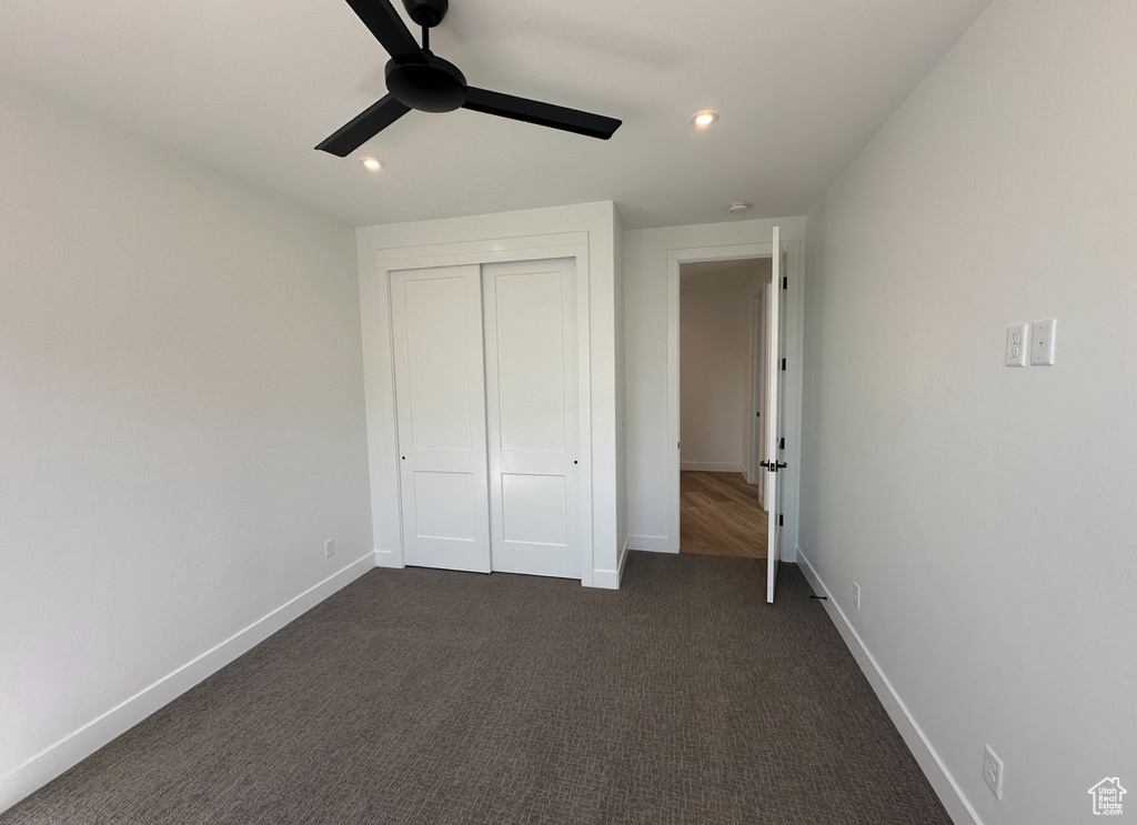 Unfurnished bedroom with a closet, ceiling fan, and dark colored carpet