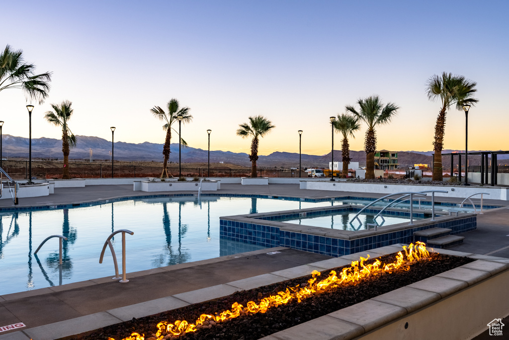 Pool at dusk featuring a mountain view, a community hot tub, and an outdoor fire pit