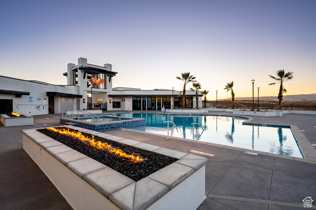 Pool at dusk with a patio, an outdoor fire pit, and a community hot tub