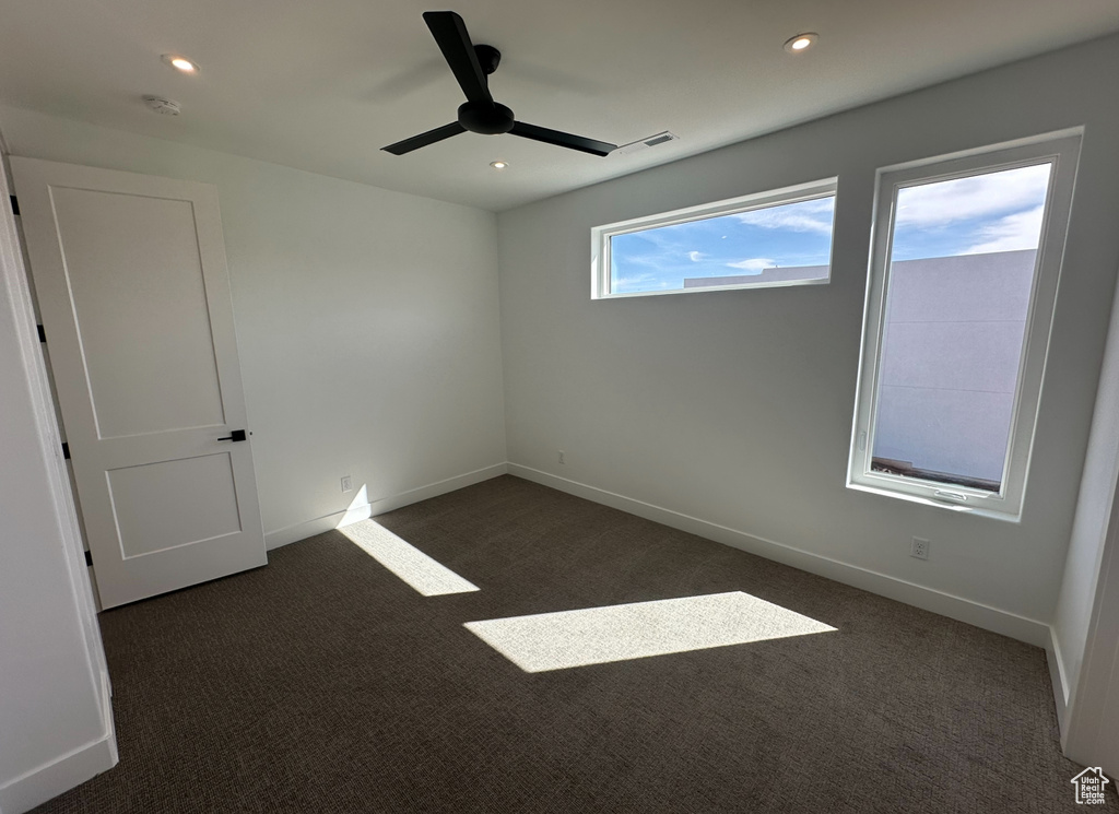 Empty room featuring dark carpet, ceiling fan, and a healthy amount of sunlight