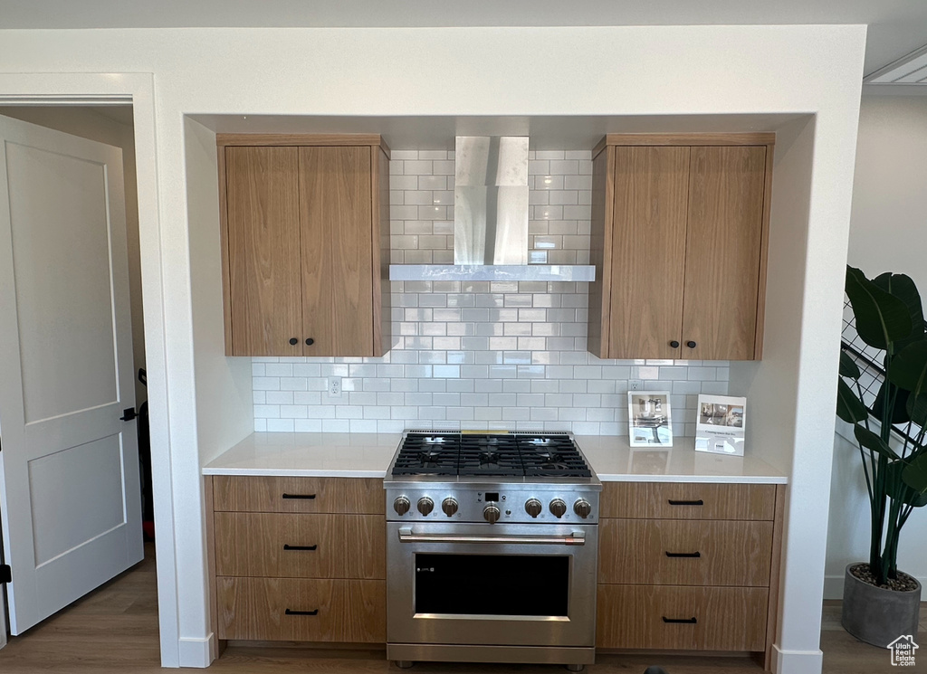 Kitchen with backsplash, hardwood / wood-style floors, wall chimney range hood, and luxury range