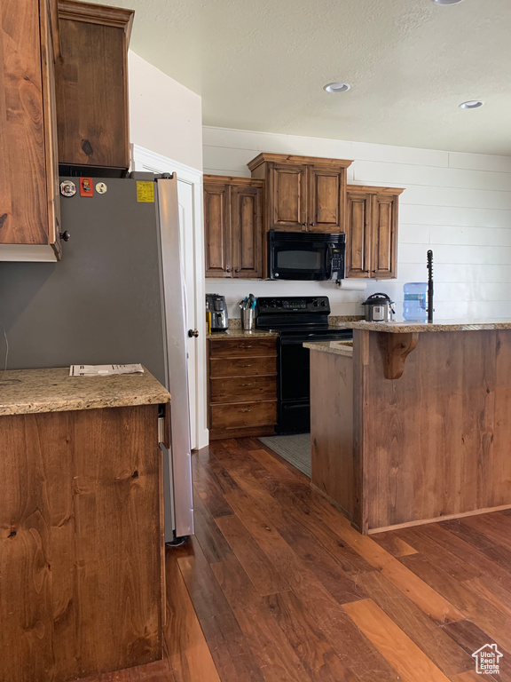 Kitchen featuring dark hardwood / wood-style floors, a breakfast bar area, light stone countertops, and black appliances