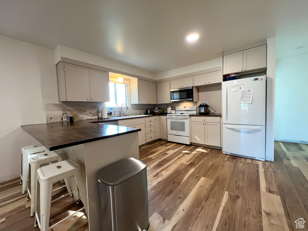 Kitchen featuring hardwood / wood-style floors, white appliances, kitchen peninsula, and a kitchen breakfast bar