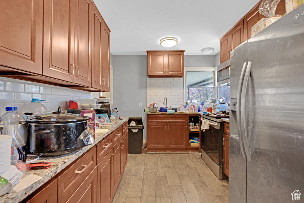 Kitchen featuring appliances with stainless steel finishes, tasteful backsplash, light hardwood / wood-style flooring, and light stone countertops