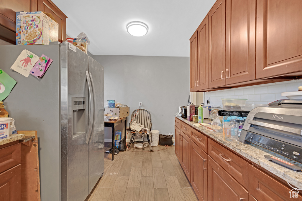 Kitchen featuring light hardwood / wood-style floors, tasteful backsplash, stainless steel refrigerator with ice dispenser, and light stone countertops