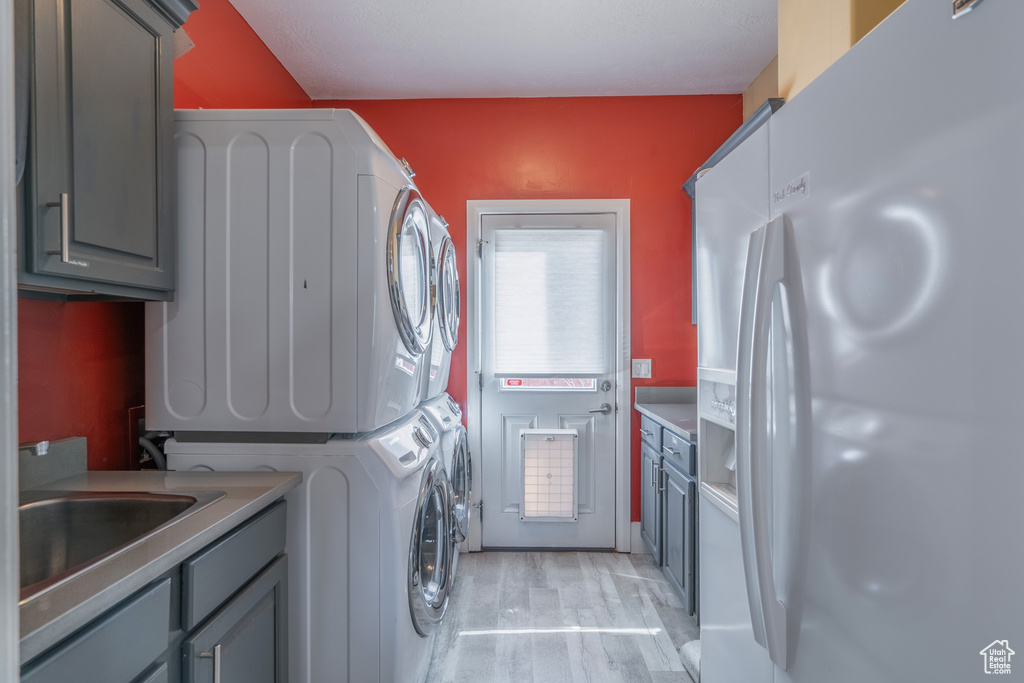 Washroom with cabinets, light hardwood / wood-style floors, stacked washer and dryer, and sink