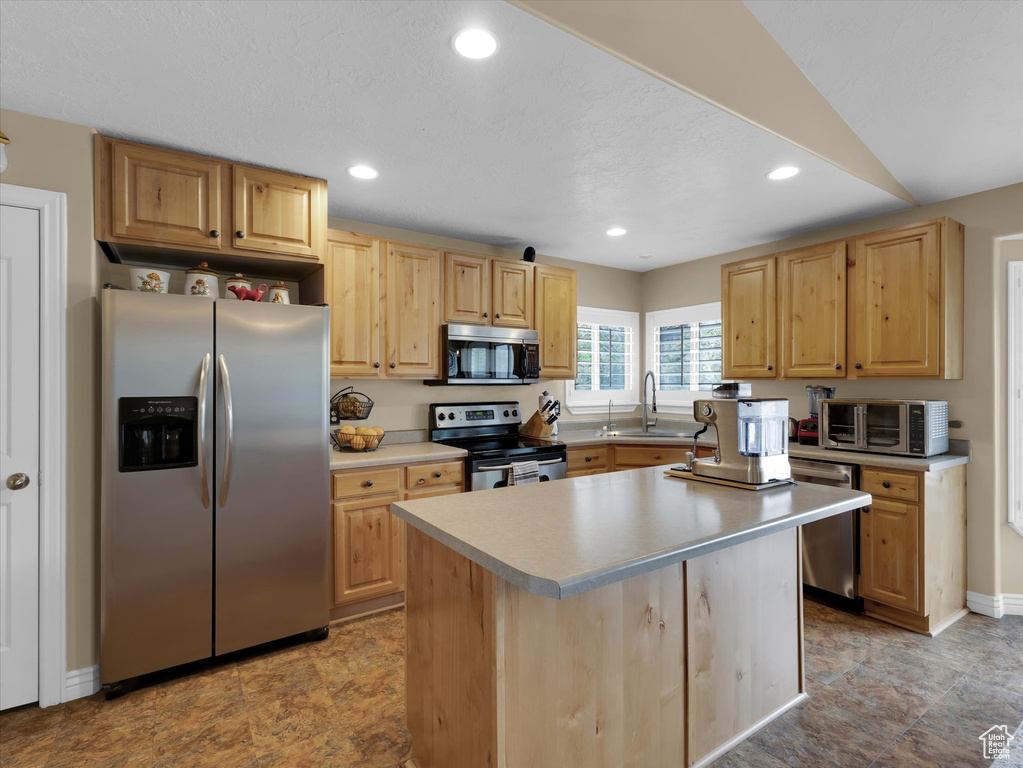 Kitchen featuring light brown cabinets, appliances with stainless steel finishes, a kitchen island, sink, and light tile floors