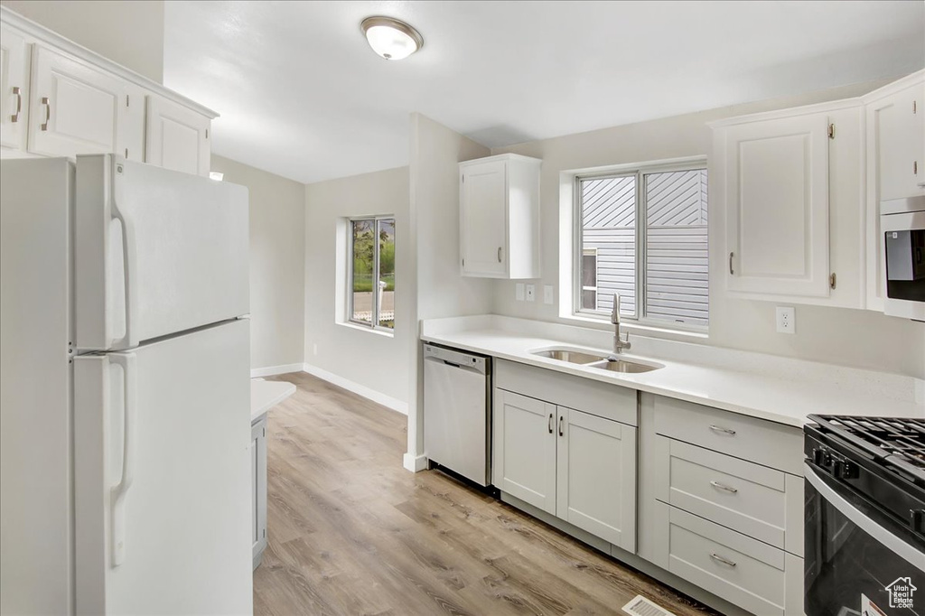 Kitchen with sink, appliances with stainless steel finishes, white cabinetry, and light hardwood / wood-style flooring