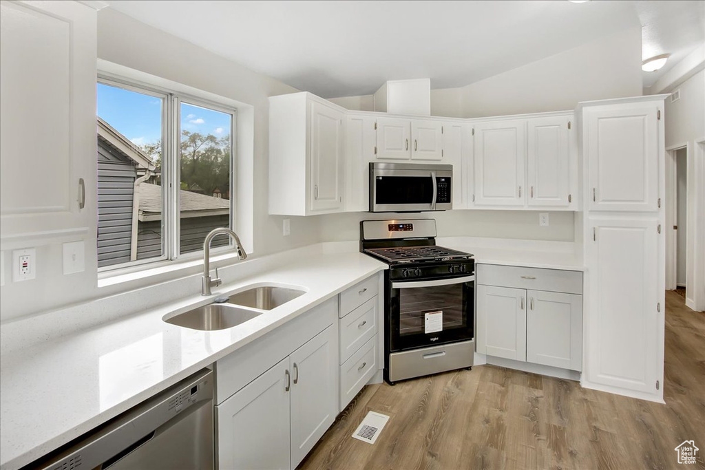 Kitchen featuring white cabinets, sink, light wood-type flooring, lofted ceiling, and stainless steel appliances