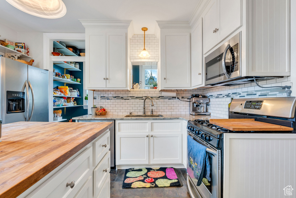 Kitchen featuring butcher block counters, backsplash, stainless steel appliances, dark tile flooring, and sink