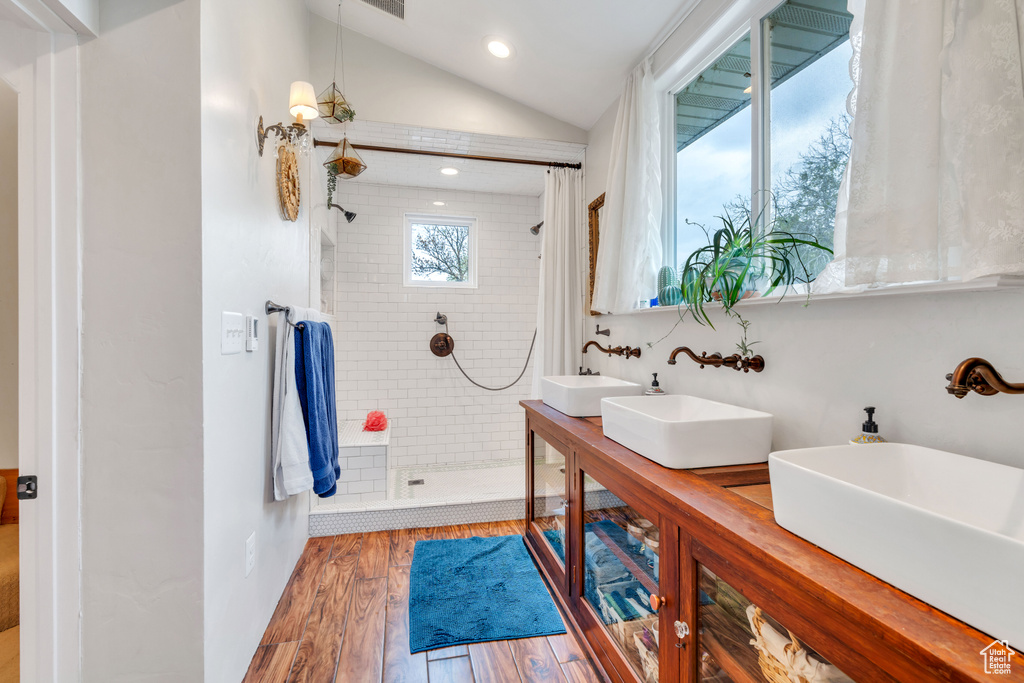 Bathroom featuring lofted ceiling, hardwood / wood-style flooring, tiled shower, and dual vanity