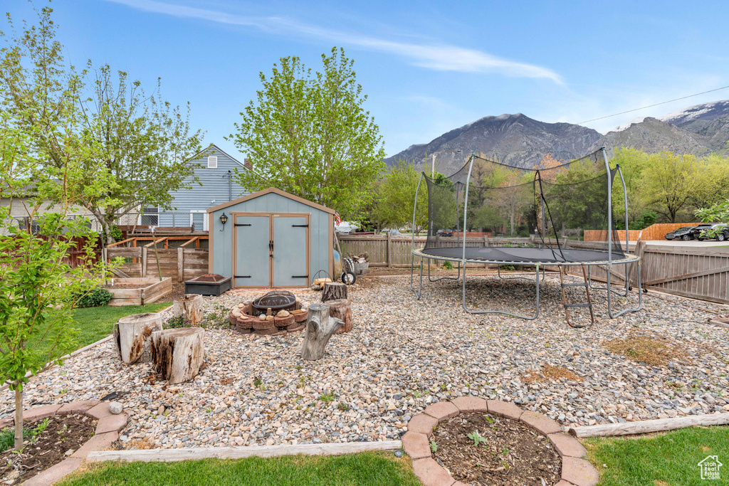 View of yard featuring a trampoline, a shed, an outdoor fire pit, and a deck with mountain view