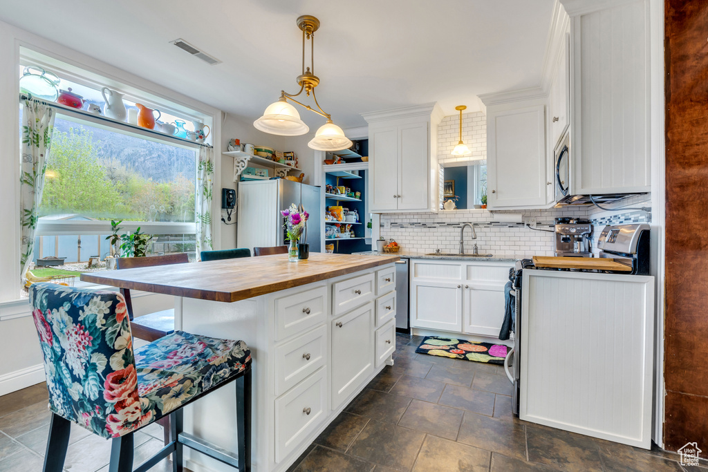 Kitchen with dark tile floors, stainless steel appliances, butcher block countertops, a kitchen island, and tasteful backsplash