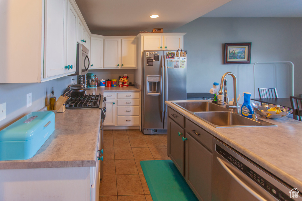 Kitchen featuring appliances with stainless steel finishes, white cabinets, sink, and light tile flooring