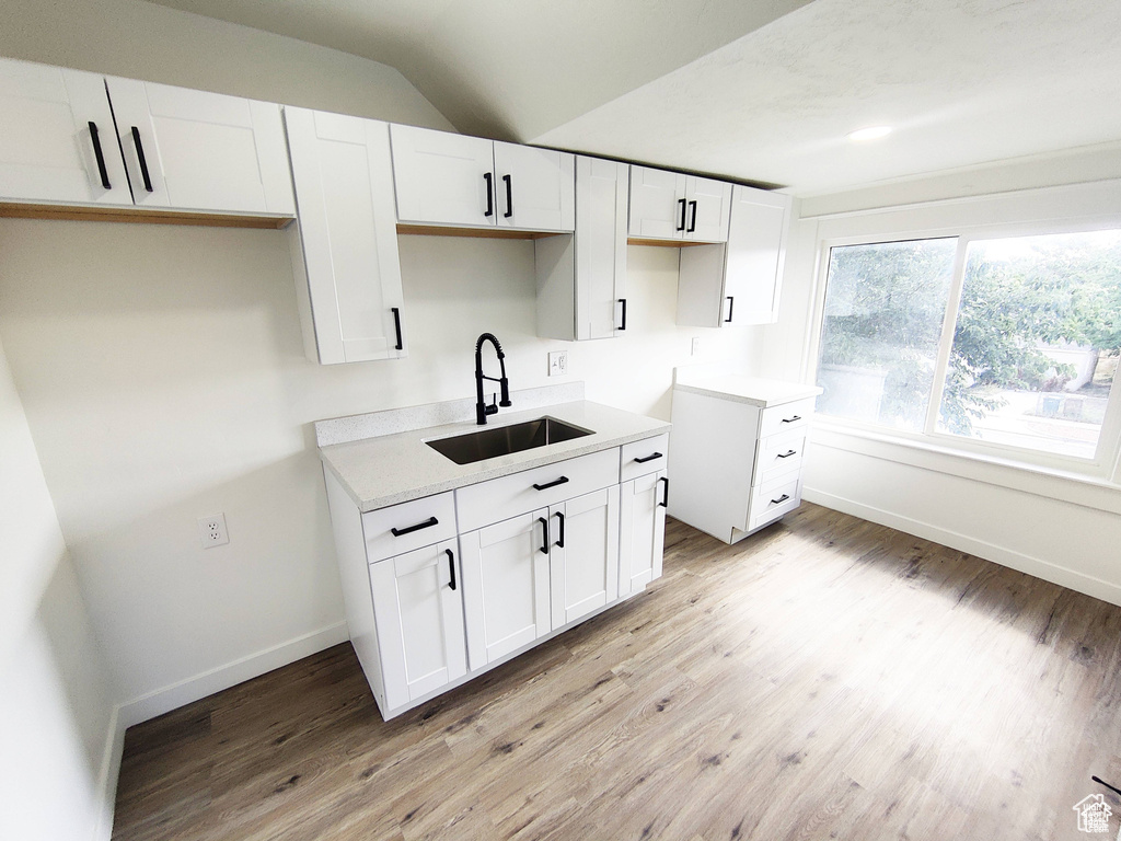 Kitchen with light hardwood / wood-style floors, white cabinets, sink, and lofted ceiling
