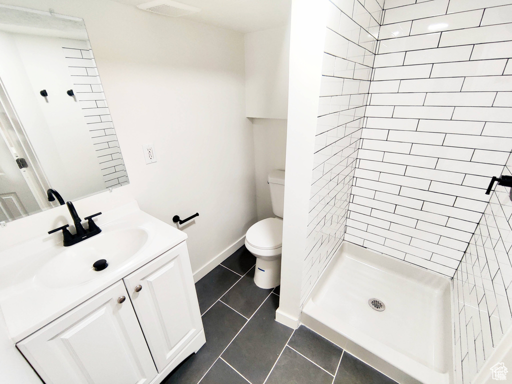 Bathroom with tile flooring, vanity, a tile shower, and toilet