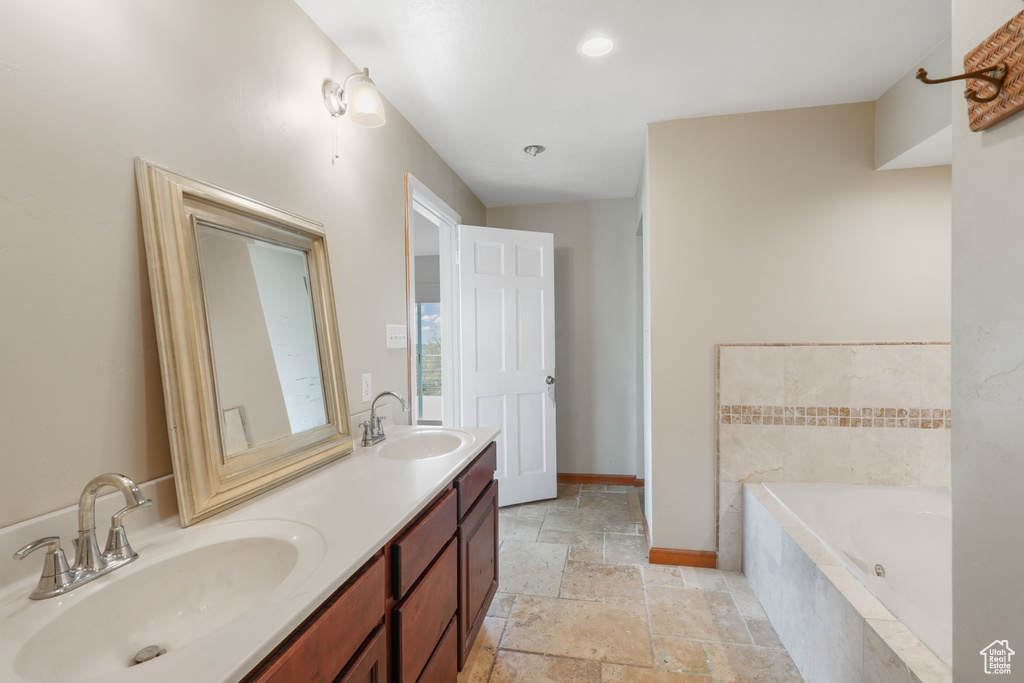 Bathroom featuring dual bowl vanity, tile floors, and tiled tub
