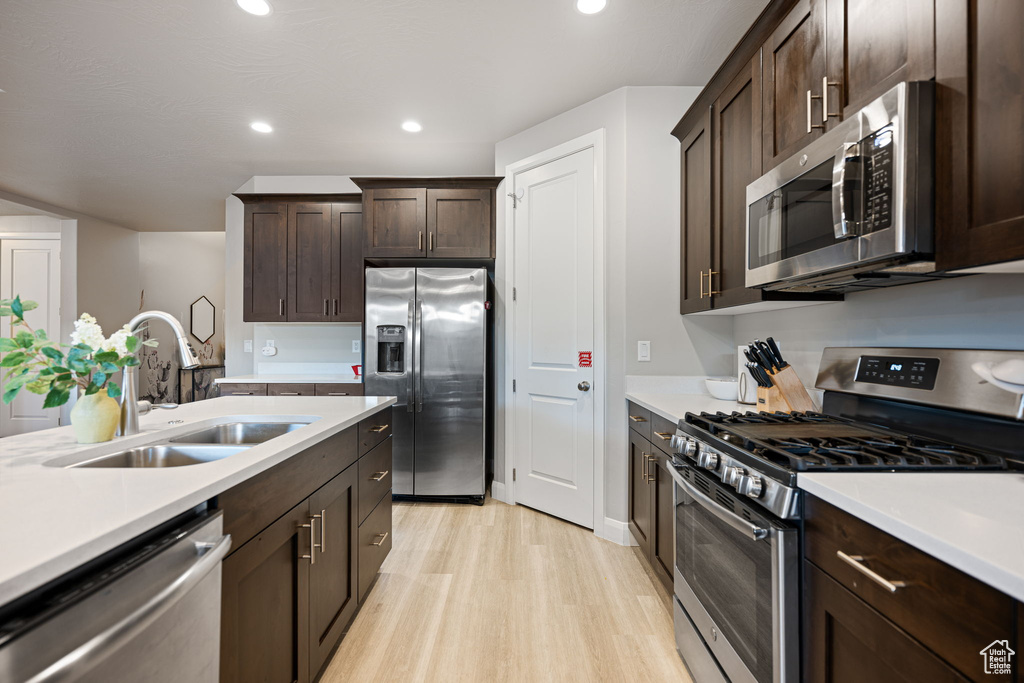 Kitchen featuring dark brown cabinetry, sink, appliances with stainless steel finishes, and light wood-type flooring