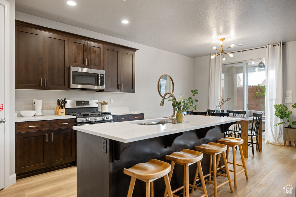 Kitchen featuring a kitchen island with sink, a chandelier, stainless steel appliances, a breakfast bar area, and light hardwood / wood-style floors