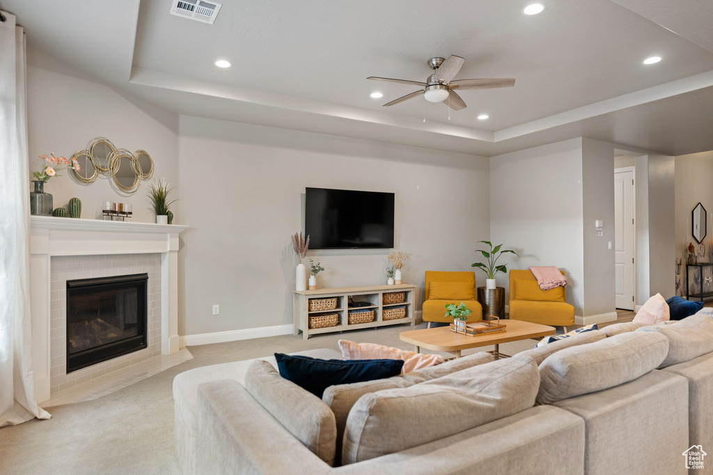 Living room with light colored carpet, a brick fireplace, ceiling fan, and a tray ceiling