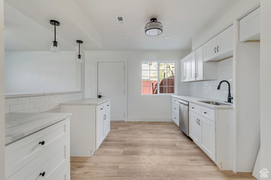 Kitchen with decorative light fixtures, light hardwood / wood-style flooring, backsplash, sink, and dishwasher